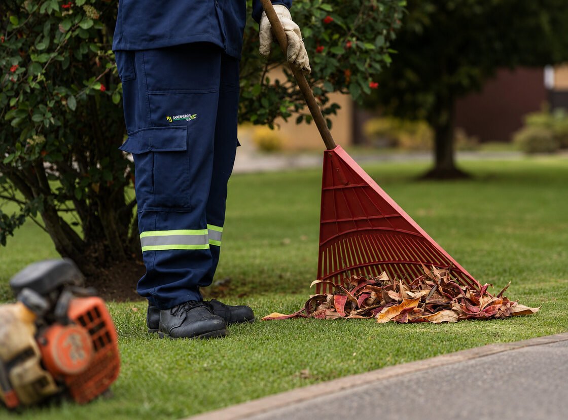 Detalle de un jardinero de RYD rastrillando hojas secas, con la motosierra en el suelo