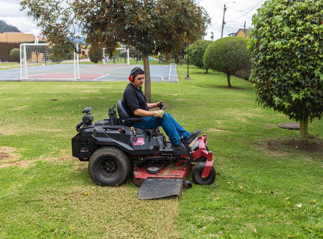 Operario de RYD cortando césped en un tractor cortacésped entre topiarios