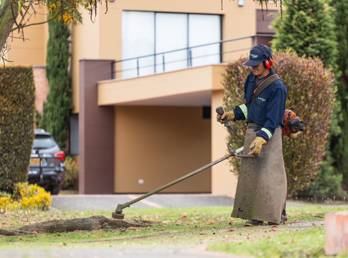 Jardinero de RYD guadañando el borde de una zona verde, con delantal y protección completa