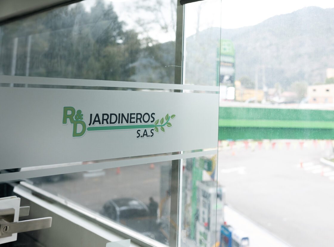 Logo R&D Jardineros grabado en el vidrio de la oficina, con la calle al fondo