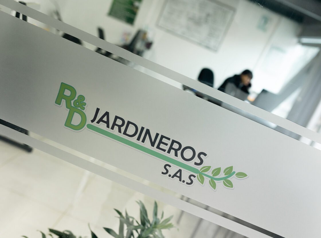 Logo R&D Jardineros S.A.S. grabado sobre la mampara de vidrio de la oficina