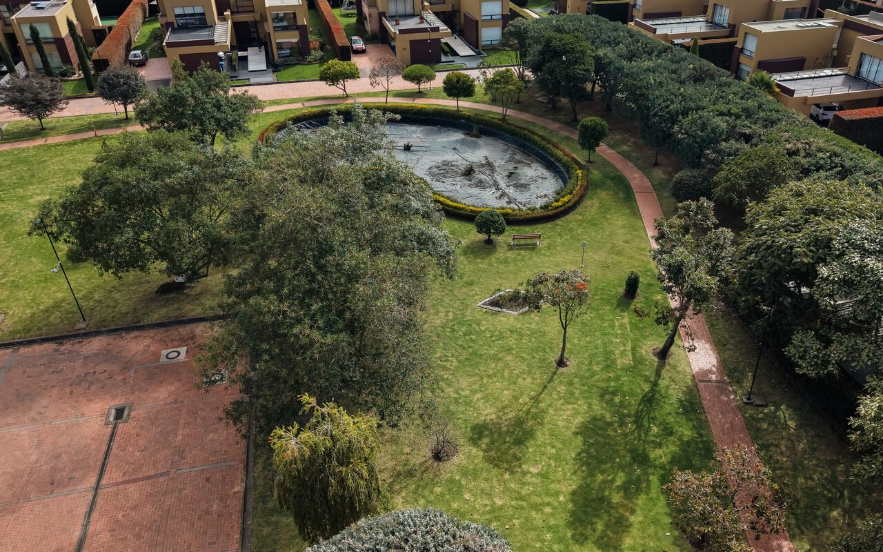 Vista aérea de una zona común con espejo de agua ovalado, arbolado y césped mantenido