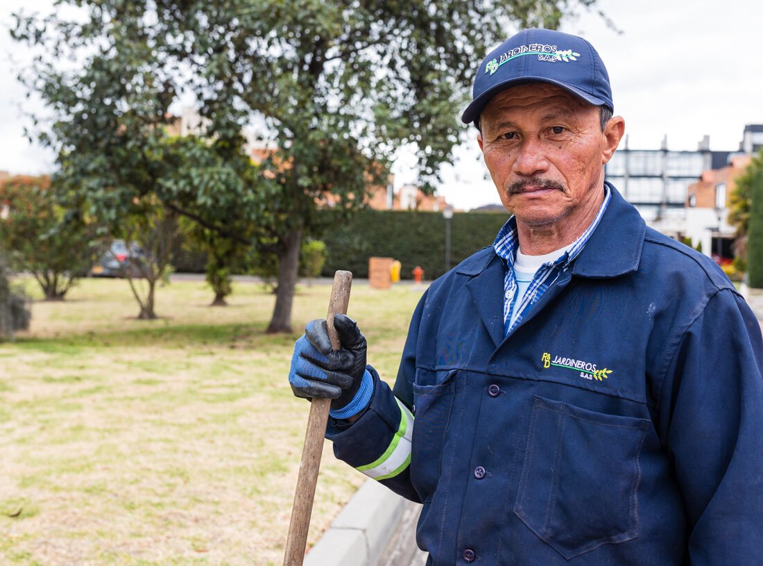 Retrato de un jardinero de RYD sosteniendo un rastrillo, en una zona verde