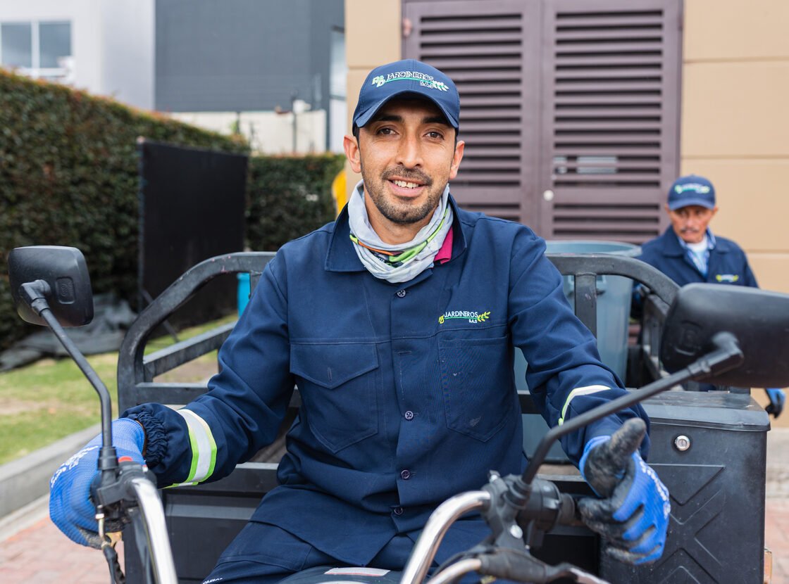 Operario de RYD en el motocarro eléctrico, con un compañero al fondo junto al cuarto de residuos
