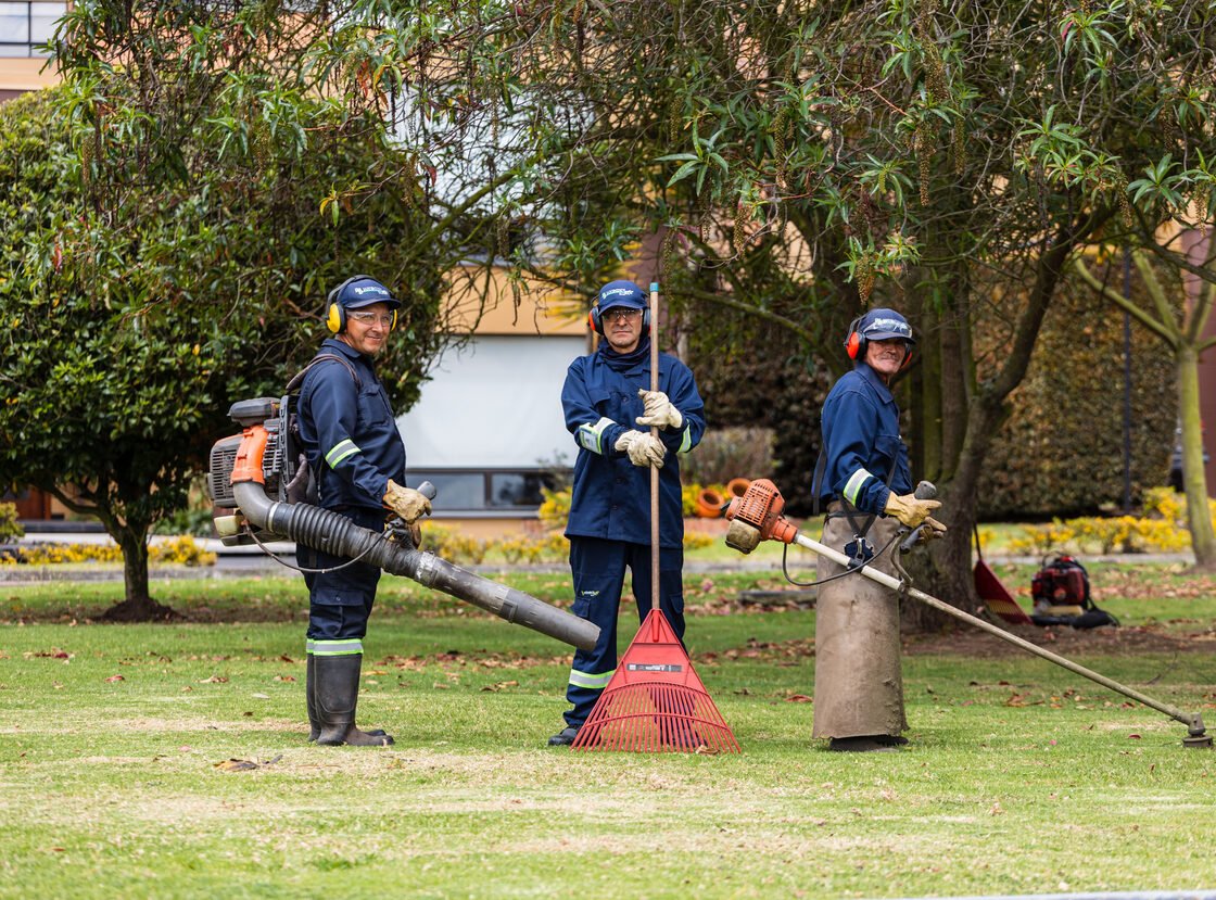 Tres jardineros de RYD con sopladora, rastrillo y guadaña, listos para una jornada de mantenimiento