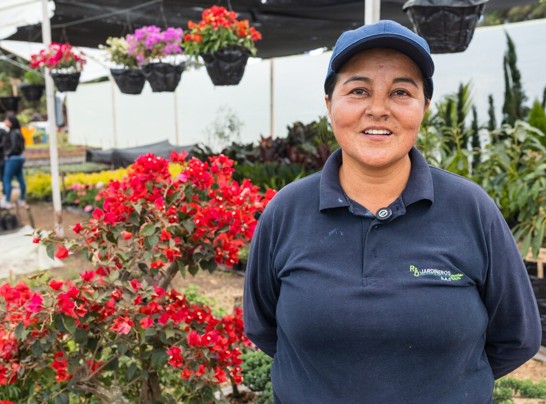 Trabajadora del vivero RYD sonriendo junto a una buganvilia roja en flor