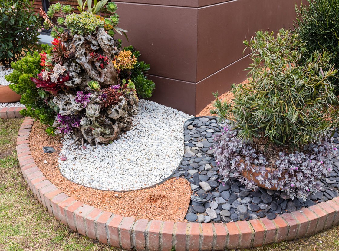 Jardinera de suculentas sobre tronco decorativo, con grava blanca, piedra negra y borde en ladrillo