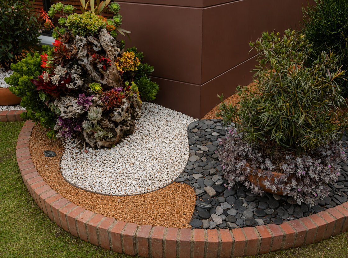 Jardinera de suculentas sobre tronco decorativo, con grava blanca, piedra negra y borde en ladrillo